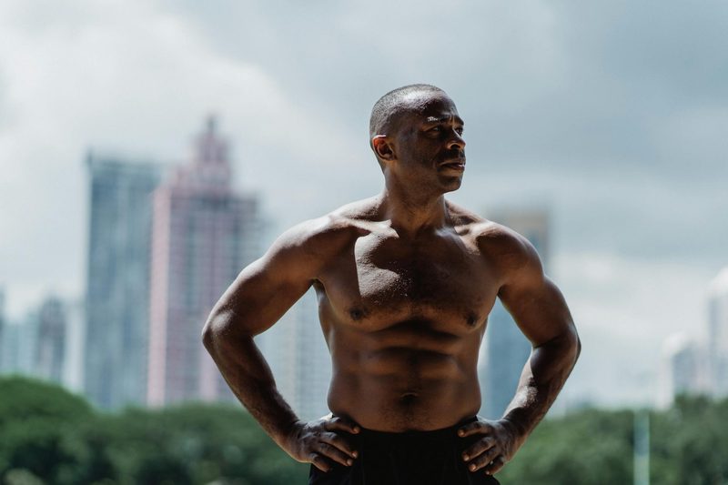 Musclular shirtless man outside with city landscape behind