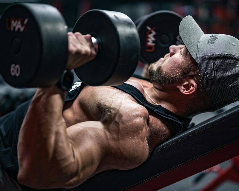 Man laying on workout bench chest pressing dumbbells