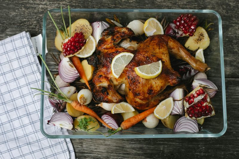 Cooked chicken in oven dish with chopped onions, herbs, and lemon.