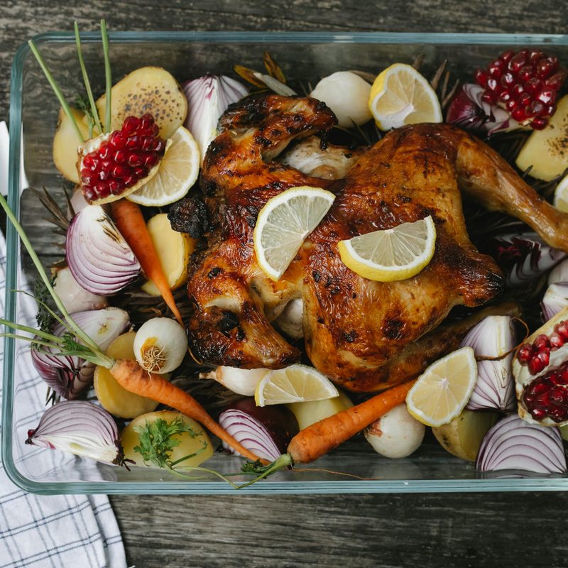 Cooked chicken in oven dish with chopped onions, herbs, and lemon.