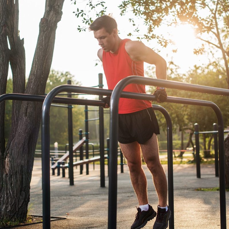 Man working out doing chest dips on parallel bars outside