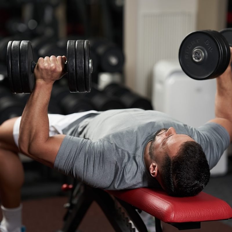 Young fitness man doing bench press with heavy dumbbells for chest workout