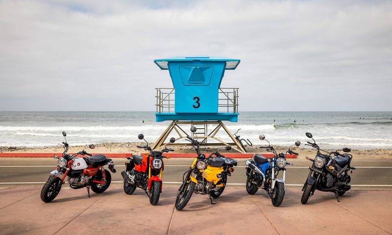 2025 Honda miniMOTO family motorcycles parked on the beach with a lifeguard stand and the ocean in the background.
