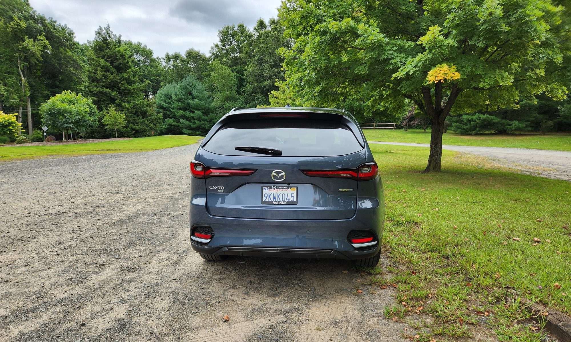 2025 Mazda CX-70 PHEV rear view parked in gravel lot surrounded by trees.