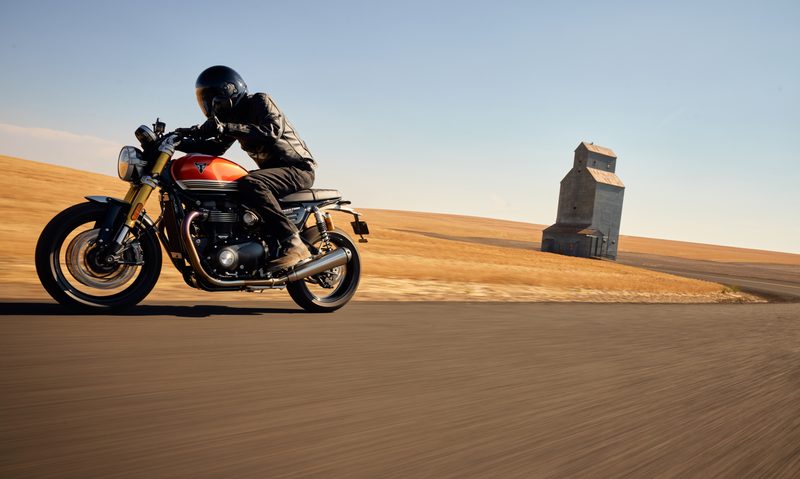 2025 Triumph Speed Twin 1200 RS tucked in riding on a curved road through farm land.