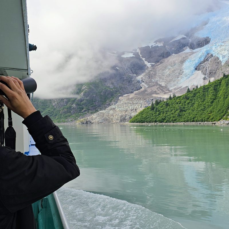 A man looking through binoculars at a glacier in Alaska