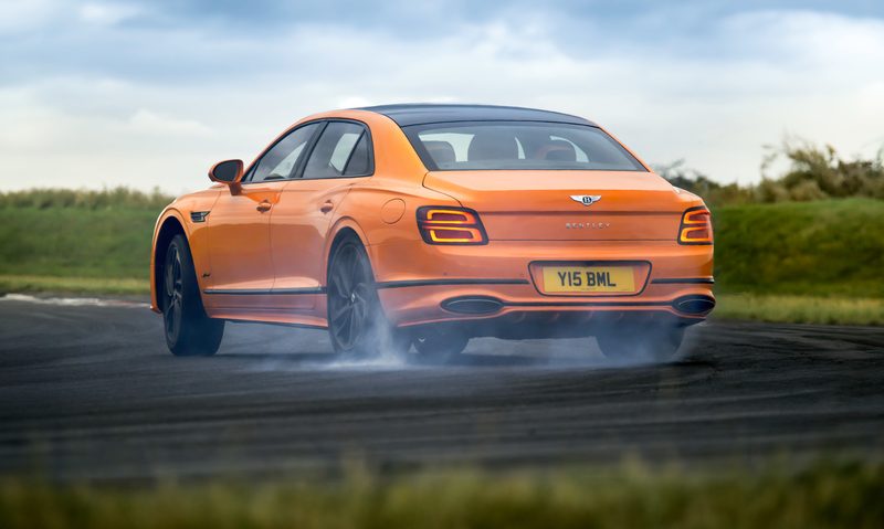 Bentley Flying Spur tease left rear three-quarter view drifting on a highway under a dark cloudy sky.