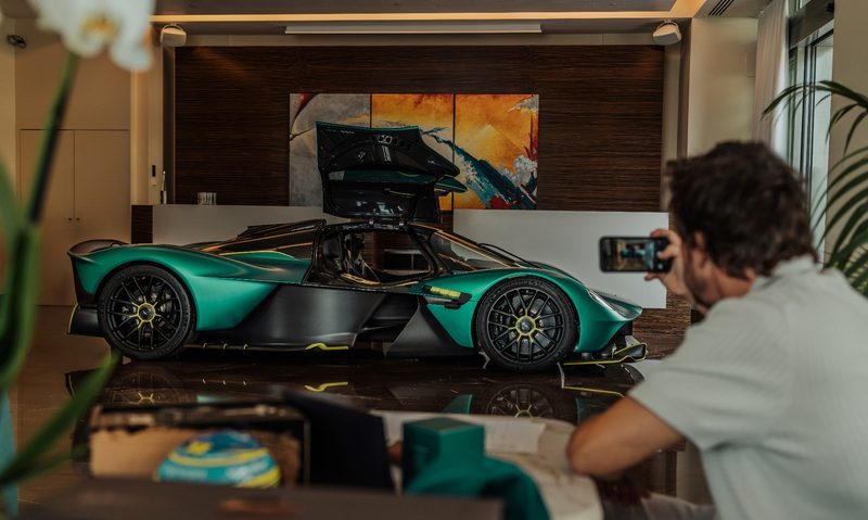 F1 driver Fernando Alonso taking a photo of his personal Aston Martin Valkyrie, right side view in a showroom.