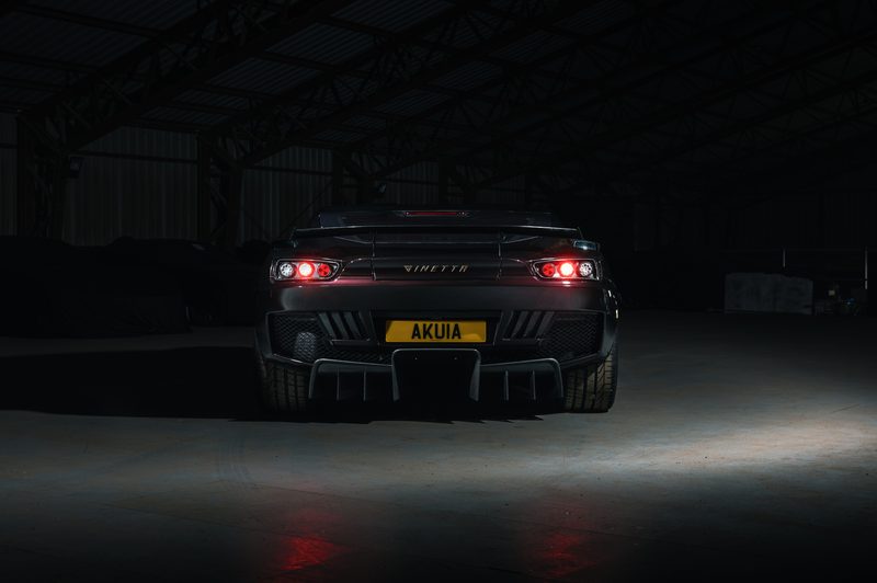 Ginetta Akula supercar for the road driver parked in a dark warehouse rear view.