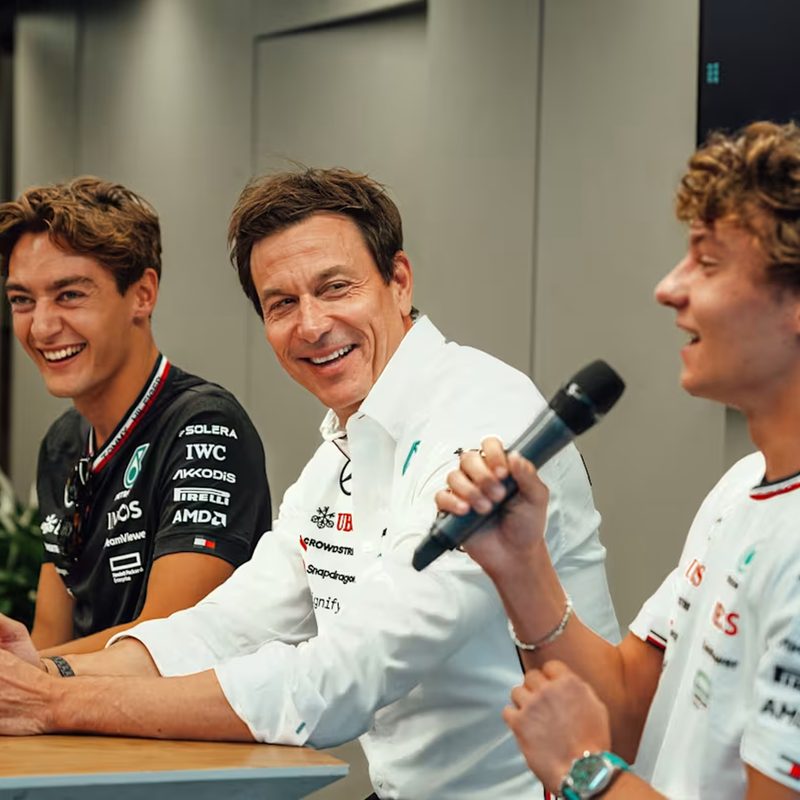 Mercedes F1 driver George Russell, Team Principal Toto Wolf, and new driver Kimi Antonelli seated at a press conference.