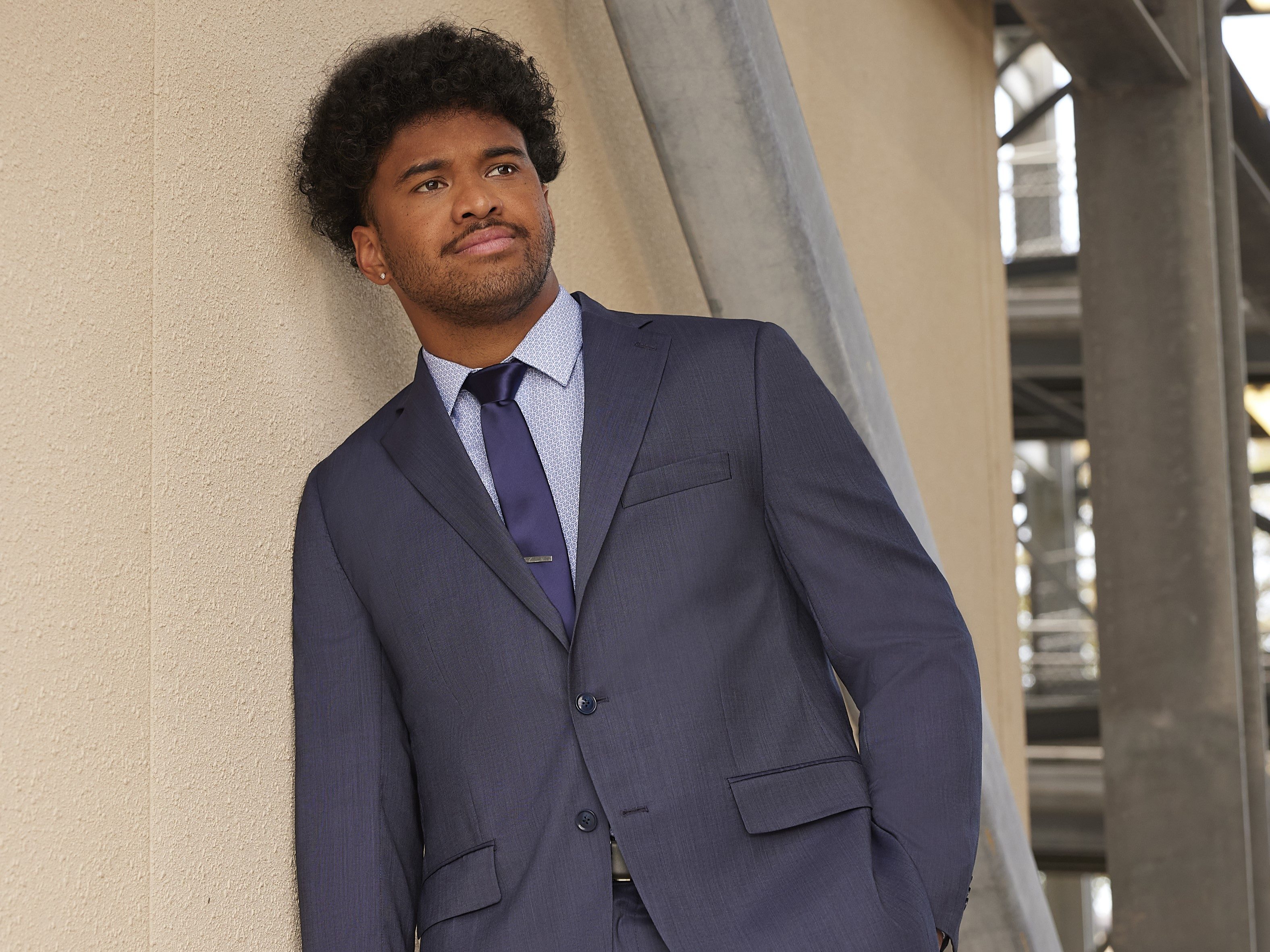 Tua Tagovailoa with his Perry Ellis collection suit leaning against a wall