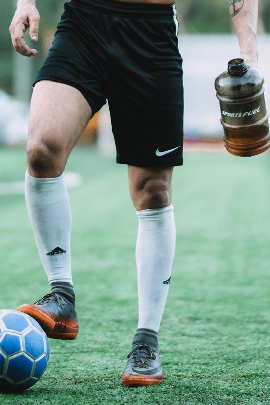 Shirtless man black shorts outside playing football on field with ball and water bottle