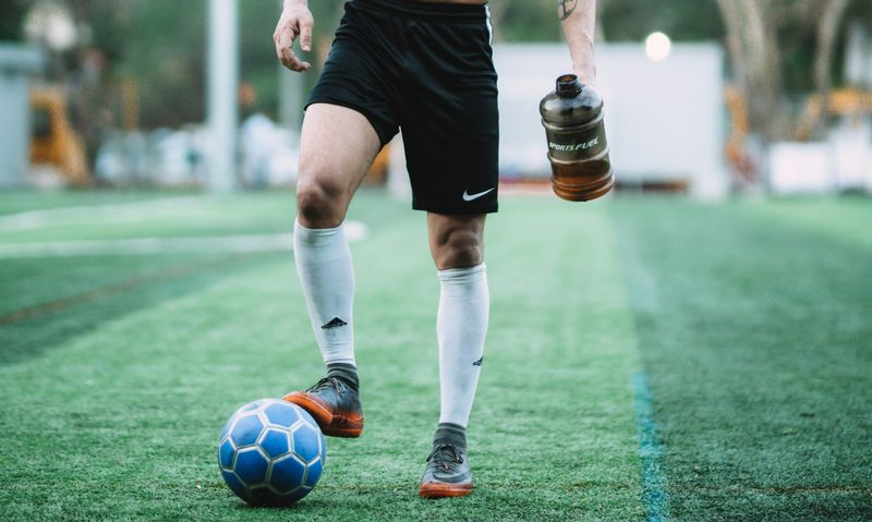Shirtless man black shorts outside playing football on field with ball and water bottle