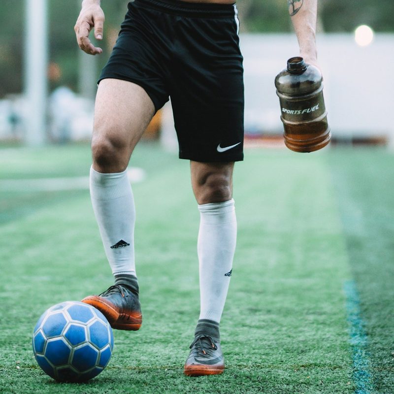 Shirtless man black shorts outside playing football on field with ball and water bottle