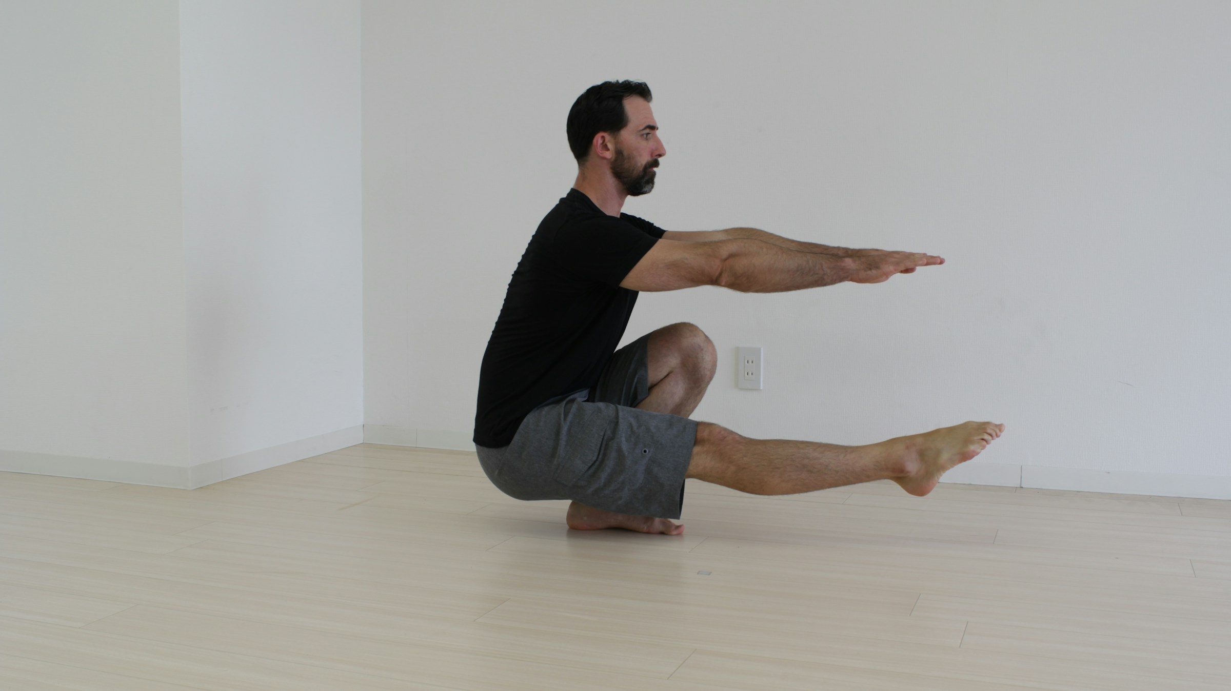 man black T shirt doing pistol squat inside on wooden floor