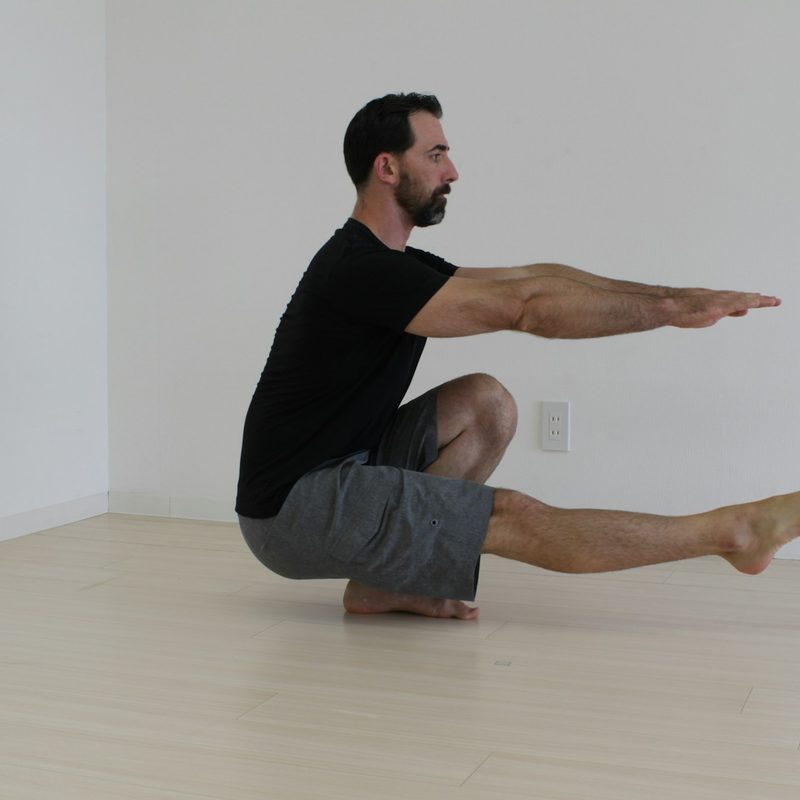 Man in a black T-shirt doing pistol squat inside on wooden floor