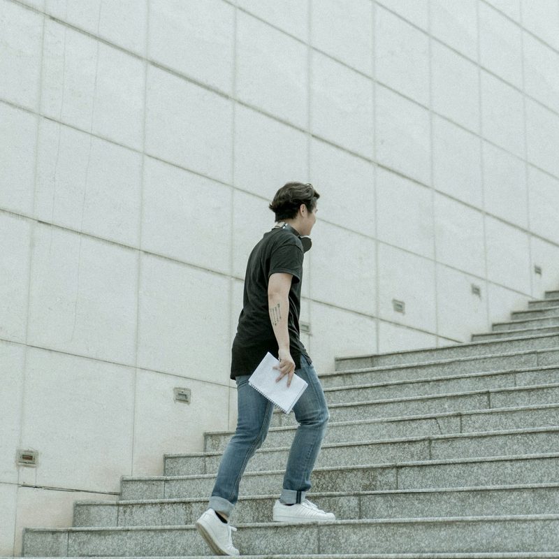 Man walking up stairs wearing jeans and white sneakers outside concrete