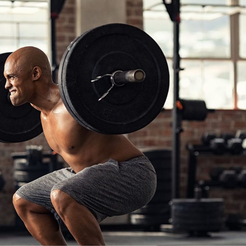 Man doing a squat with barbell wearing gray shorts