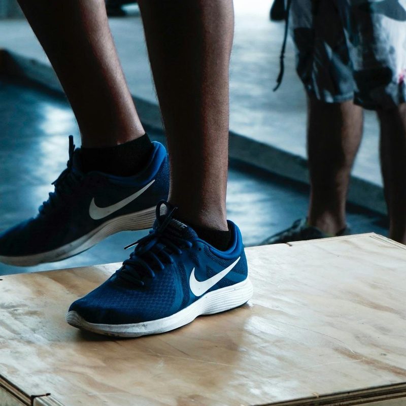 Close-up man legs wearing blue sneakers doing step-up exercise in gym