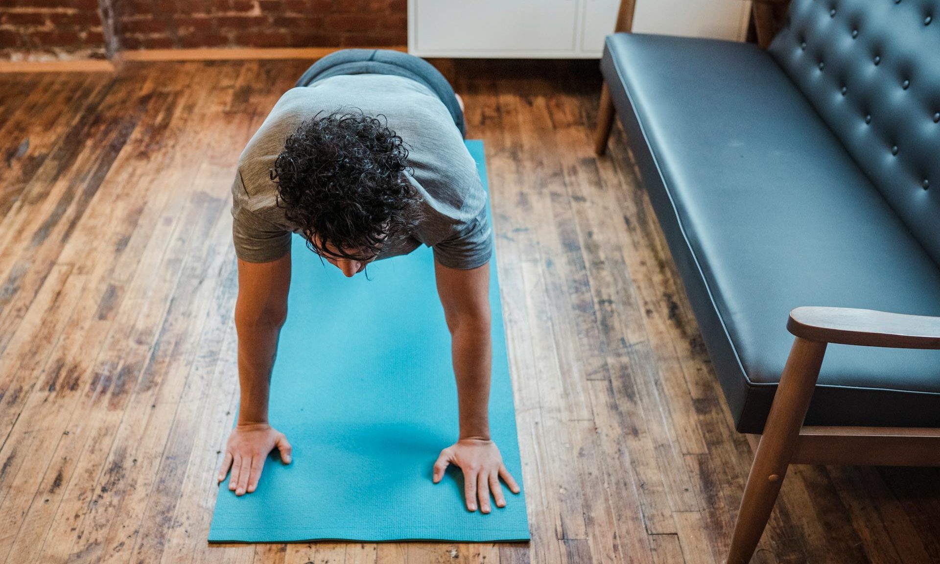Man doing yoga plank pose at home on blue yoga mat on a wooden floor