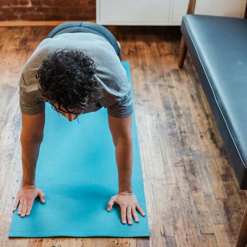 Man doing yoga plank pose at home on blue yoga mat on a wooden floor