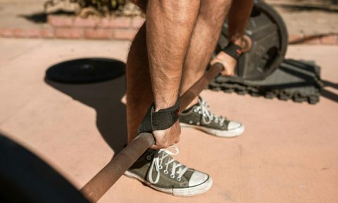 close up of mans hands picking up barbell bent-over barbell row on floor outside