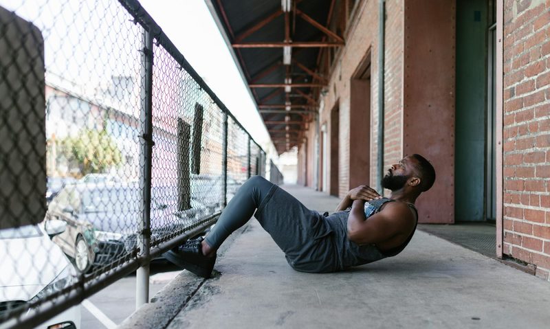 Man doing situps using a fence for help outside on a concrete floor
