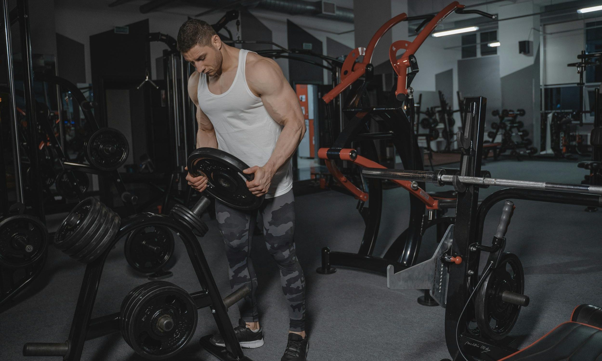 man wearing white tank top in gym holding weight stacking weights on rack in gym