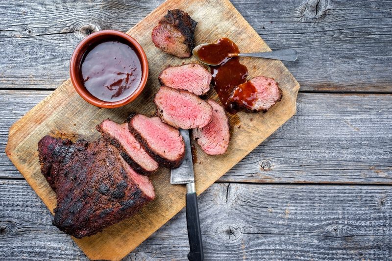 Barbecue dry-aged wagyu tri-tip steak with BBQ sauce as dip as top view on a wooden cutting board