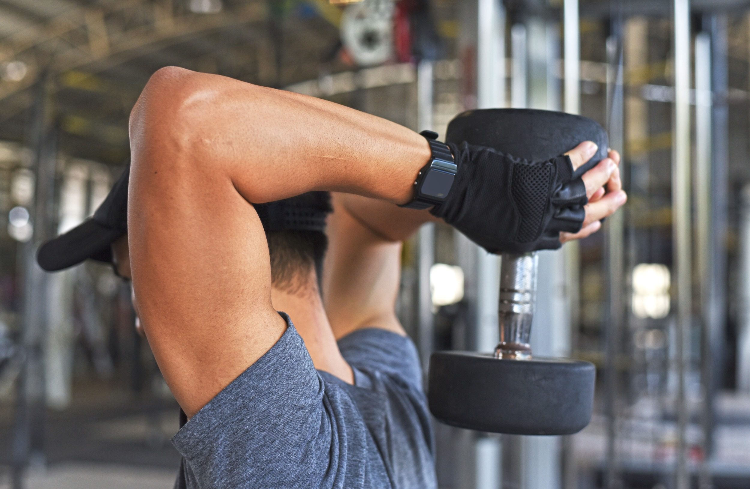 man black hat blue t shirt overhead tricep extension with dumbbell in gym