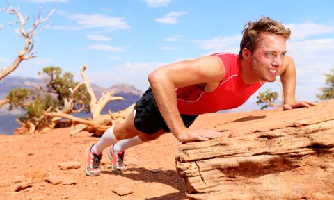 man red shirt outside blue sky doing incline push up on a log