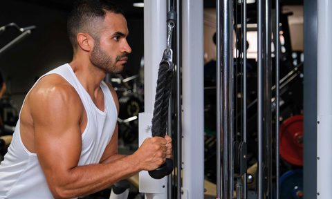 Man wearing tank top doing cable pullover exercise in gym with cable machine