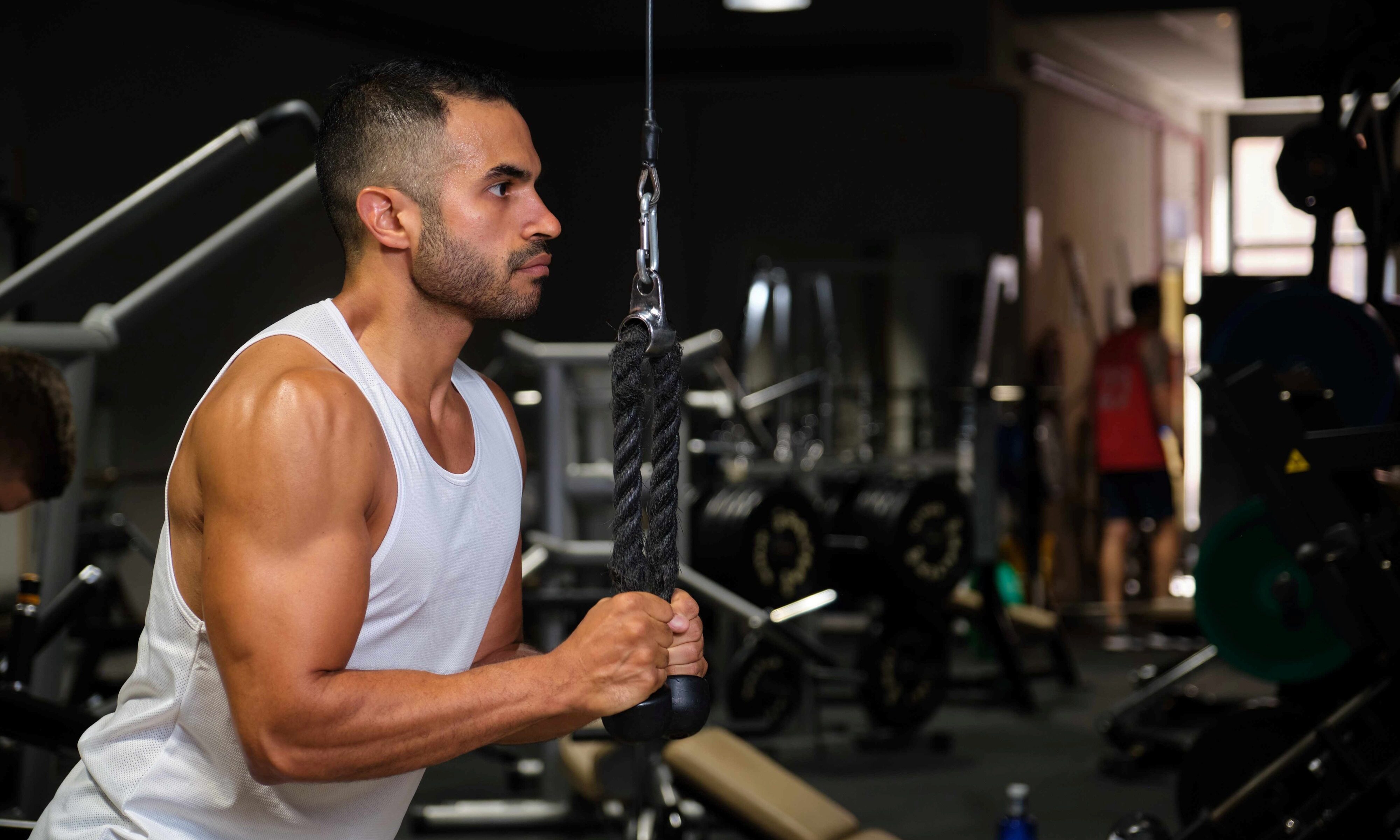 Man wearing tank top in gym doing cable pullover exercise on cable machine rope pulley
