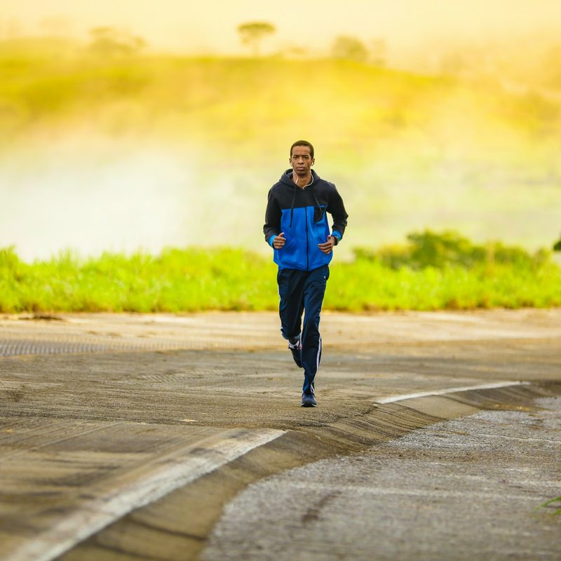 man wearing black and blue jacket running outdoors in nature
