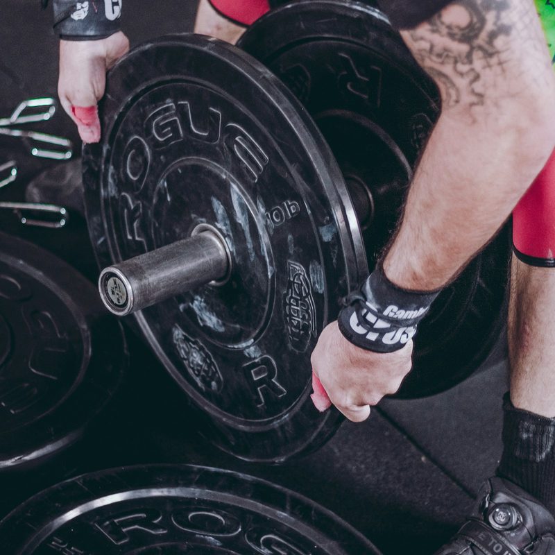 Close-up of a man leaning down putting weights on barbell stacking weights on end of barbell