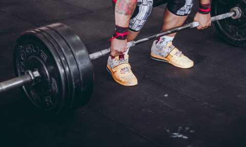 Man bending down to pick up barbell for bent-over barbell row close up of feet and hands and barbell