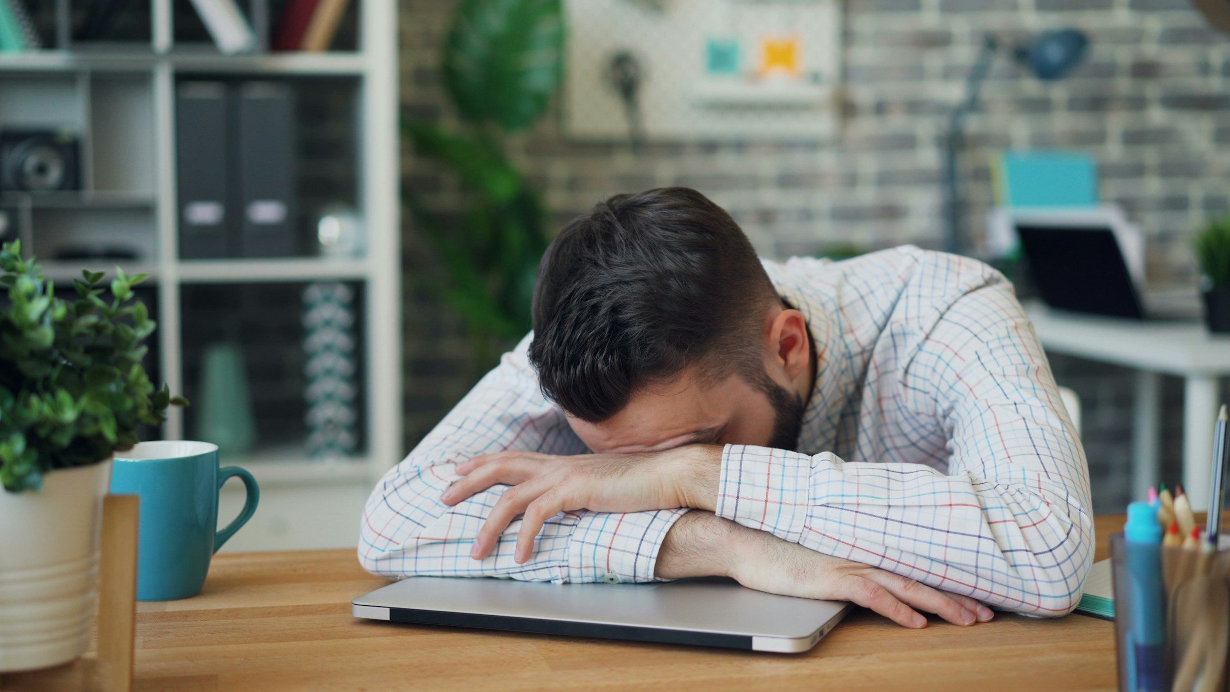daily grind man head in arms hands on desk laptop tired sleepy