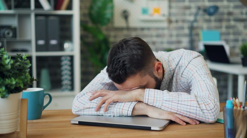 Daily grind man head in arms hands on desk laptop tired sleepy