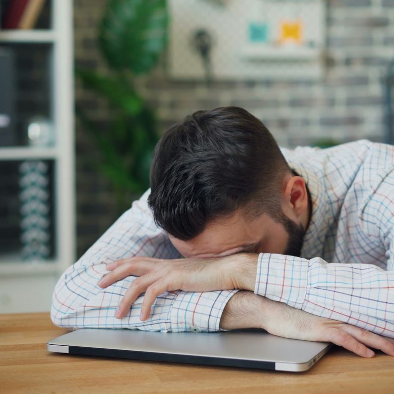 Daily grind man head in arms hands on desk laptop tired sleepy