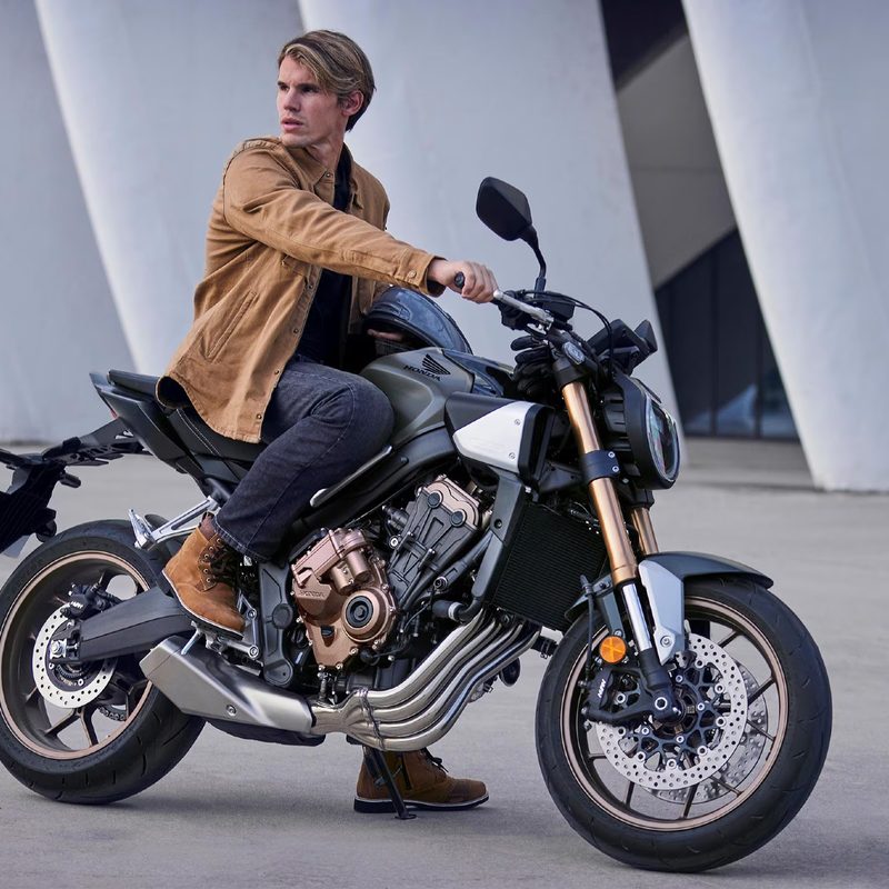 A person on a Honda CB650R stopped on concrete next to a modern building