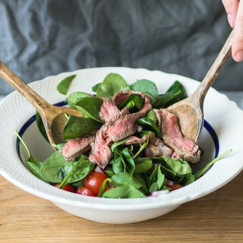Person tossing steak salad