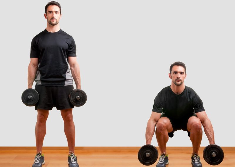 Man wearing black T-shirt doing dumbbell squat exercise on wooden floor