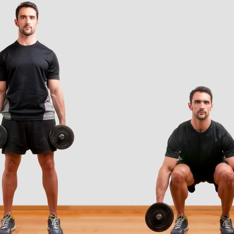 Man wearing black T-shirt doing dumbbell squat exercise on wooden floor