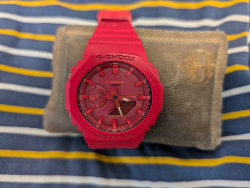 A red Casio G-Shock GA-2100 strapped around a wallet, sitting on a shirt.