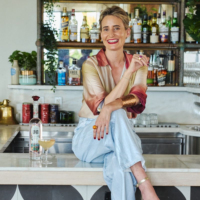 Leticia Fernández de Mesa founder of UNA Vodka sitting atop a bar - Photo Credit Michael Pisarri
