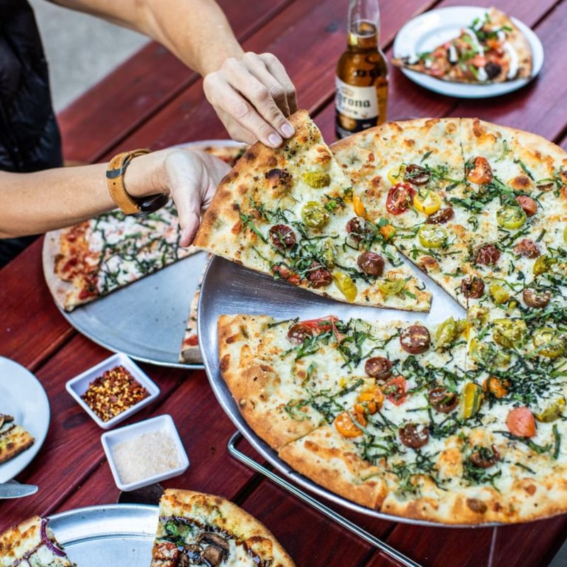 A full pizza with a person removing a single slice