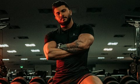 Strong man standing in the gym arms folded leaning on weight rack