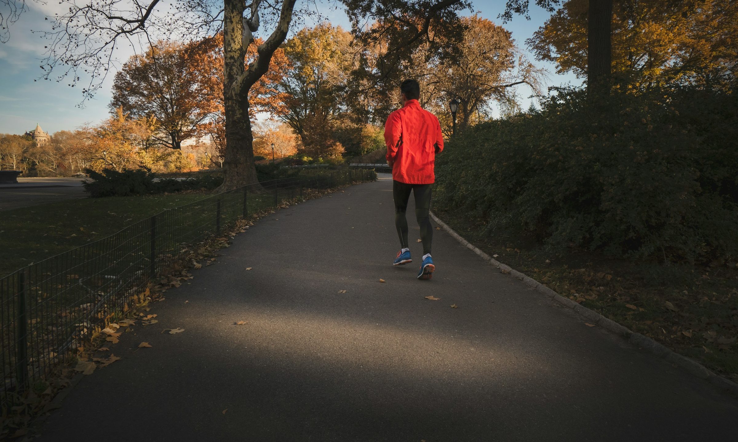 man running through trees on path wearing red jacket