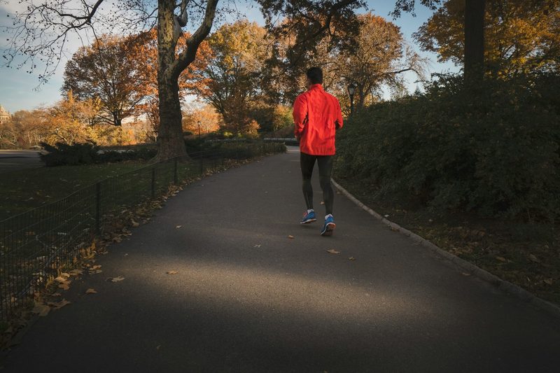 man running through trees on path wearing red jacket