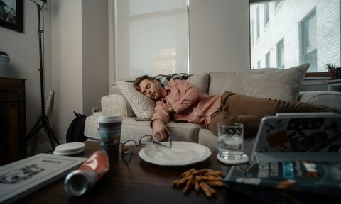 man laying on couch sleeping with messy table empty food plates glasses